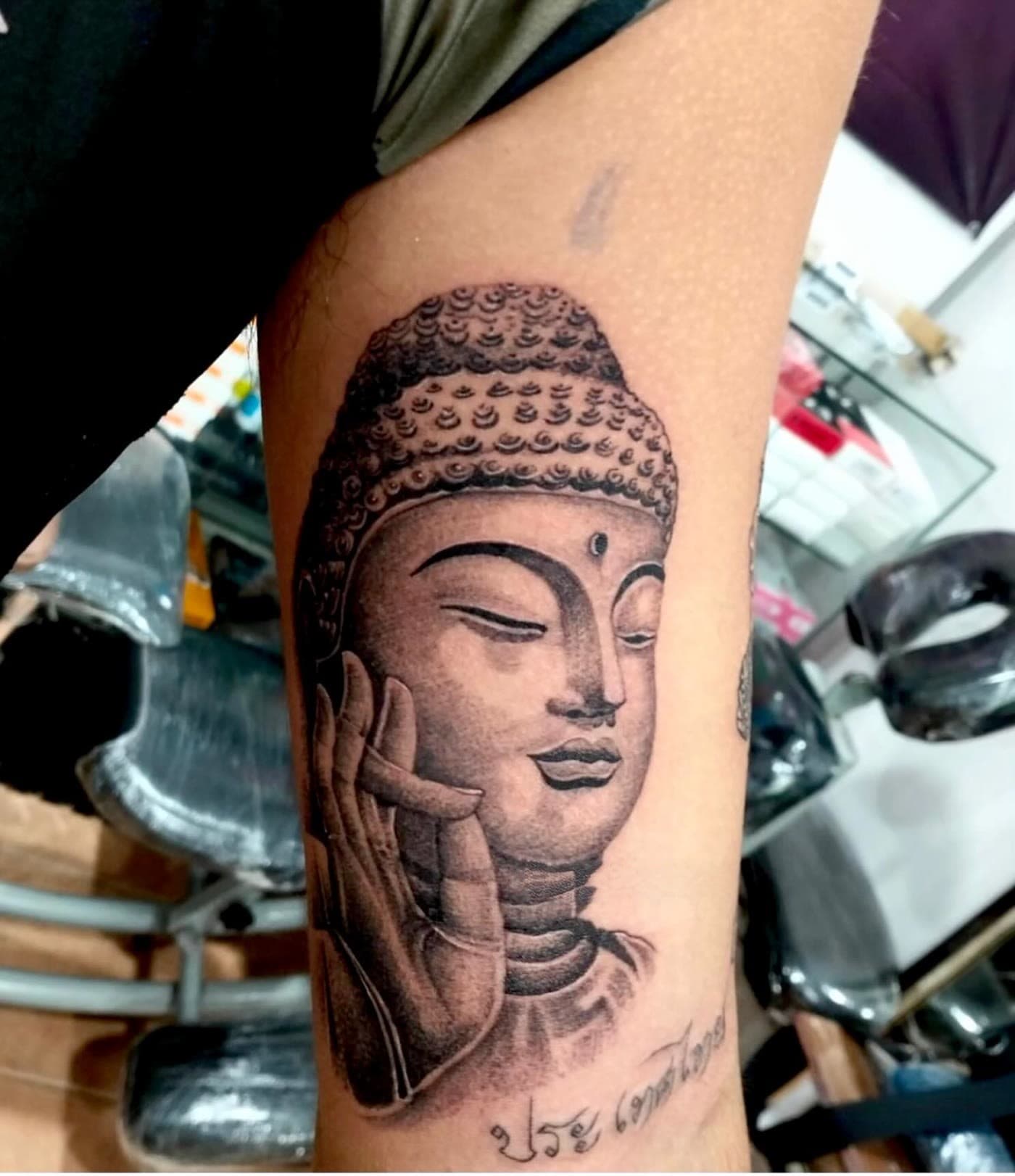 Realistic Buddha face tattoo on the upper arm